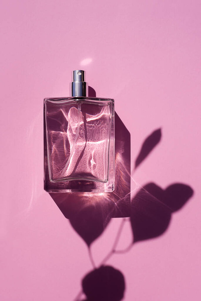 Transparent bottle of perfume on a pink background. Fragrance presentation with daylight. Trending concept in natural materials with eucalyptus leaves shadow. Women's and men's essence. - Photo, image
