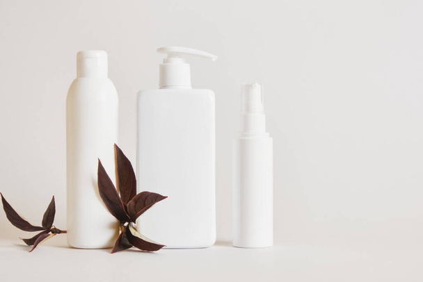 blank white bottles for cosmetics, mock up cream jar and autumn branch with leaves on a beige light background, packaging for cosmetics without logo and label - Foto, afbeelding