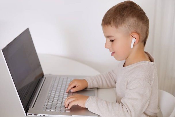 Evde dizüstü bilgisayarda oyun oynayan küçük mutlu çocuk. Evde bilgisayarda çizgi film izleyen bir çocuğun portresi. Modern çocuk ve eğitim teknolojisi. - Fotoğraf, Görsel