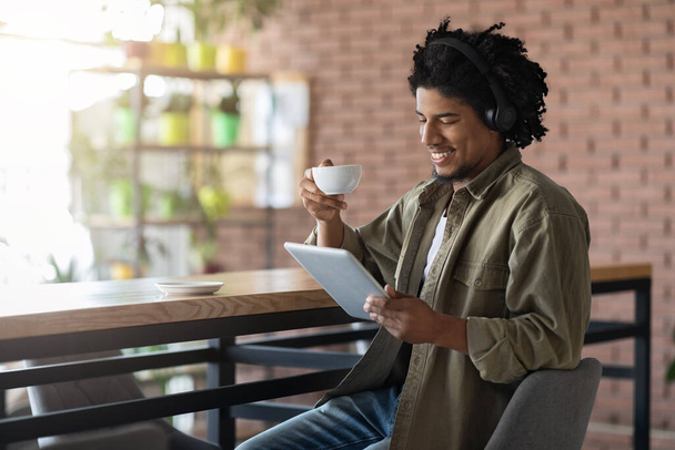 ヘッドフォンで黒男デジタルタブレットとカフェでコーヒーとリラックス - 写真・画像