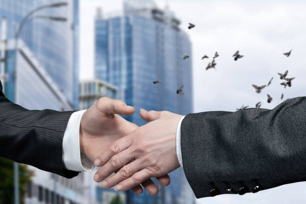 Business cooperation concept. Businessmen hold out their hands for a handshake on the background of the business center. - Photo, Image