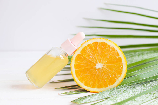 Bottle of cosmetic skincare serum with dropper, orange and palm leaf. Citrus essential oil with Vitamin C. Selective focus. Beauty and spa concept - Foto, Bild
