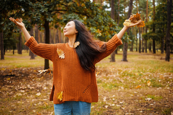 gelukkig aziatische vrouw gooien bladeren in herfst park. - Foto, afbeelding