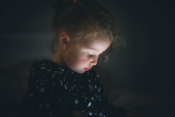 Menina criança com tablet em um quarto escuro. - Foto, Imagem