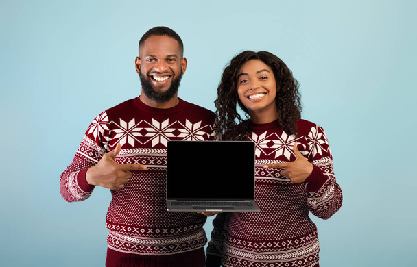 Weihnachtseinkauf im Internet. Glückliches afrikanisch-amerikanisches Paar zeigt Laptop mit leerem Bildschirm und zeigt darauf - Foto, Bild