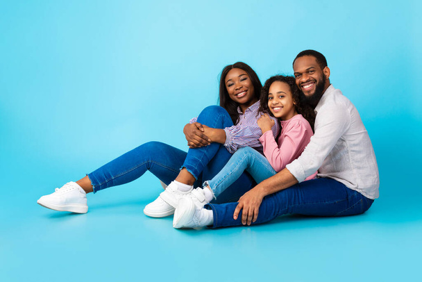 Homem negro abraçando sorridente esposa e filha, sentado no chão - Foto, Imagem