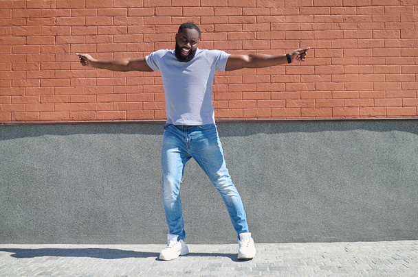 A dark-skinned man in a white tshirt and jeans feeling good - 写真・画像