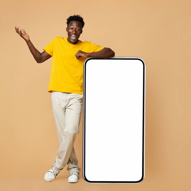 Surprised Young Black Guy Standing Next To Big Smartphone With White Screen - Valokuva, kuva