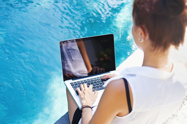 Woman working on laptop at poolside - Foto, imagen