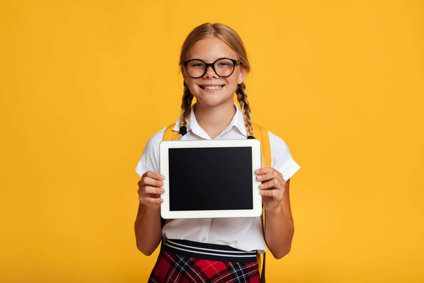 Glad adolescence blonde schoolgirl in glasses shows tablet with empty screen - Zdjęcie, obraz