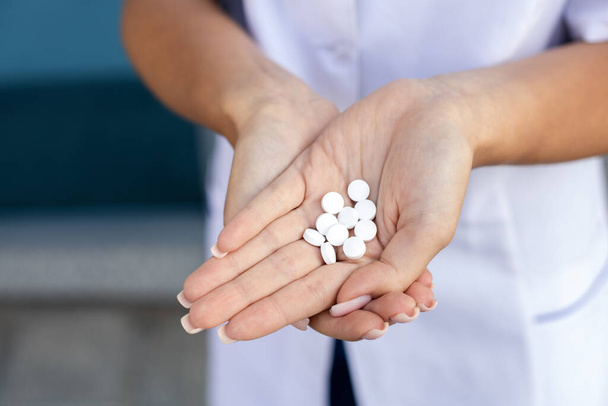 Healthcare, medicine and people concept. Oriental female hands of a social worker in a medical gown holding a handful of white pills in the palms on the street in good weather - Photo, Image