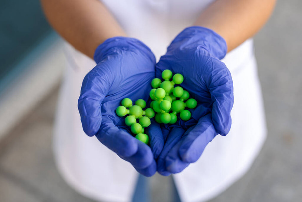 Фізика, наука, біологія та концепція медицини. Білі жіночі руки в медичних синіх рукавичках тримають готову фізичну модель зелених атомів крупним планом, показуючи її зовні
 - Фото, зображення