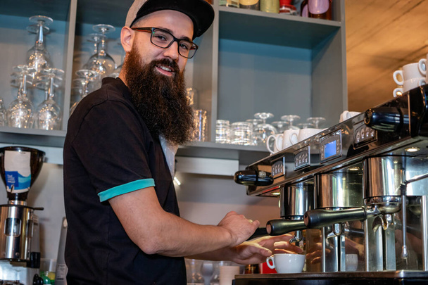 Vousatý barista dělá šálek espressa pomocí profesionálního kávovaru. Selektivní zaměření. - Fotografie, Obrázek