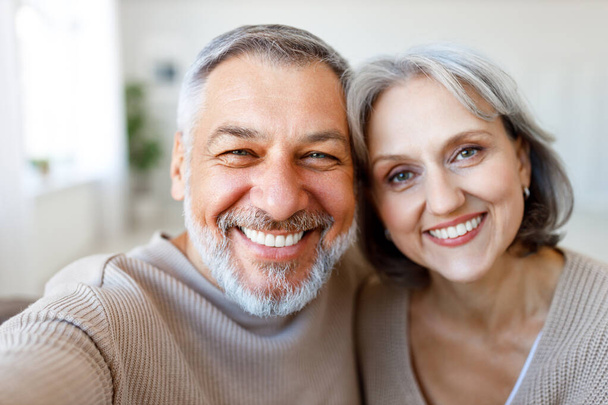 幸せな美しいシニア白人家族のカップルの肖像カメラで笑顔,明るい退職妻と夫は自宅で一緒に時間を過ごしながらスマートフォンで自画自身を作ります - 写真・画像