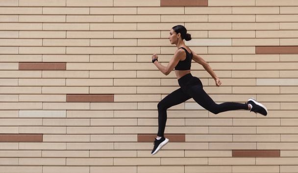 Sportovní motivace. Sportovní mladá žena v sportovním oblečení běží přes cihlové zdi na pozadí - Fotografie, Obrázek