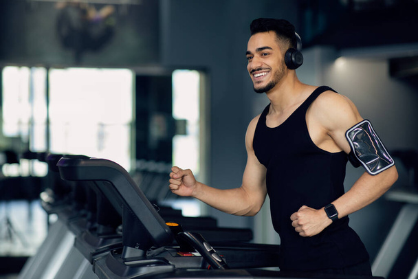 Handsome Muscular Arab Man In Wireless Headphones Jogging On Treadmill At Gym - Φωτογραφία, εικόνα
