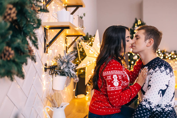 Młoda szczęśliwa para całuje się. Kobieta i mężczyzna świętują Boże Narodzenie. Wesołych Świąt. Przytulne chwile rodzinne. - Zdjęcie, obraz