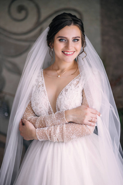 Красивая брюнетка невеста в платье и вуаль, с красивым макияжем и прической, стоит в комнате перед церемонией. - Фото, изображение