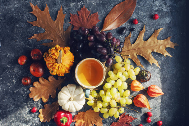 Cozy autumn composition, cup of tea,  pumpkins, grapes, autumn leaves on dark stone table, seasonal decoration for Halloween or Thanksgiving day,  - Zdjęcie, obraz