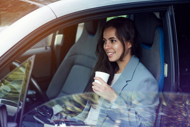 Attractive young woman taking a coffee break. Successful businesswoman with laptop, notebook and smartphone sitting in the car. - Foto, immagini