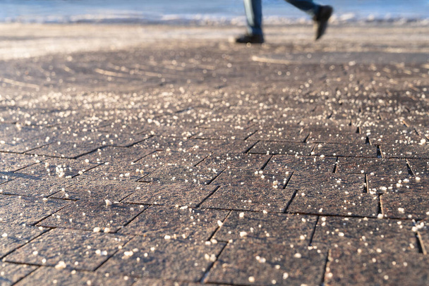 Chemische Enteisungsmittel auf der Straße machen die Straße im Winter sicher. Pflaster wird mit technischem Salz bestreut, Fokus auf Vordergrund, Menschen auf verschwommenem Hintergrund. - Foto, Bild