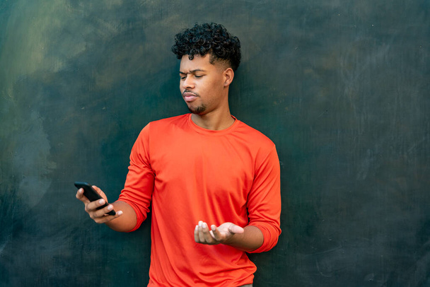 Afro latinsky mladý muž pomocí mobilního telefonu u zdi - Fotografie, Obrázek