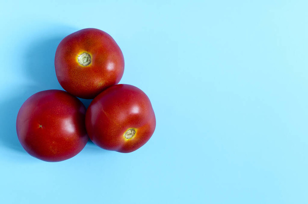 Three red tomatoes on a blue background top view. Ripe tomatoes on a colored background are a place for text. - Valokuva, kuva