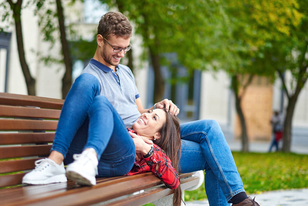 Lovely portrait of a young couple. They are sitting on the bench, embracing and kissing - Foto, afbeelding