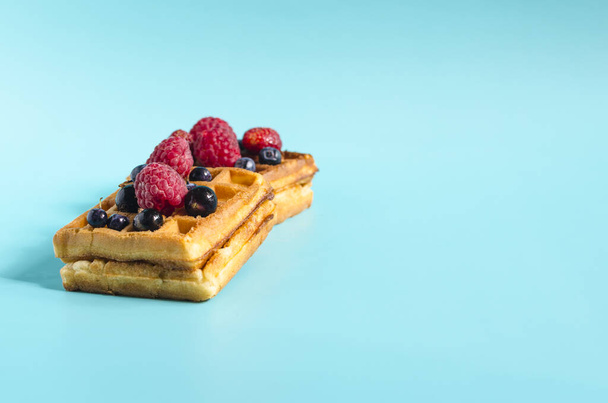 Fresh waffles with different berries of black and red color on a blue background hard light. Homemade cakes crispy waffles on a colored background copy space - Foto, afbeelding