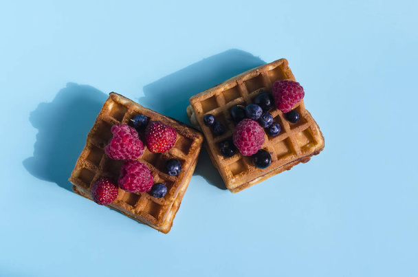 Fresh waffles with different berries of black and red color on a blue background close-up. Homemade cakes crispy waffles on a colored background - Foto, afbeelding