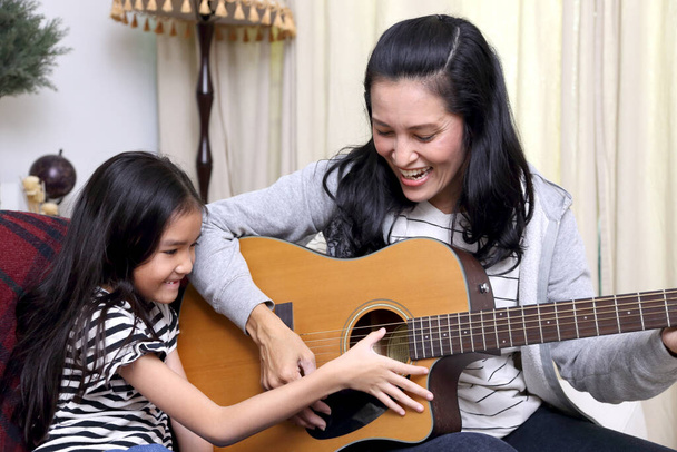 The Asian mother teaching her child to play guitar. - Foto, afbeelding