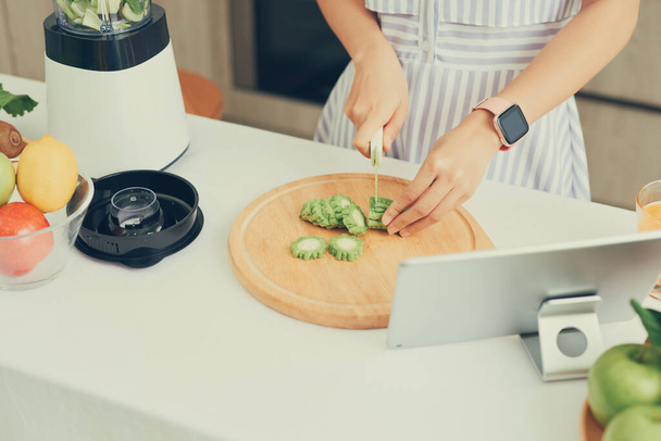 Asian woman cutting vegetables in kitchen with tablet in front of her - Photo, Image