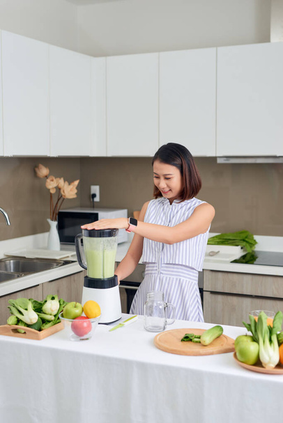 Sorridente donna asiatica vegana che fa un frullato con frutta e verdura in cucina
 - Foto, immagini
