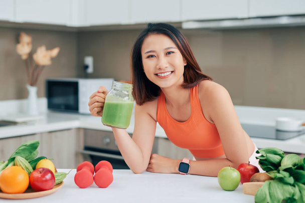 Pretty Asian woman drinking green detox juice while wearing sportive clothing - Foto, afbeelding