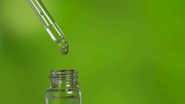 Drop falling into glass jar with medicinal liquid on green gradient background - Footage, Video