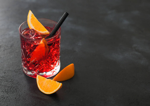 Negroni cocktail in crystal glass with orange slice and black straw on black table background. Top view - Fotoğraf, Görsel