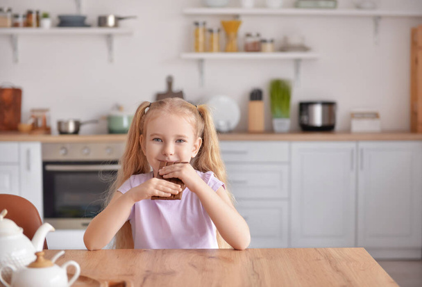 Cute little girl jedzenia słodkiej czekolady w kuchni - Zdjęcie, obraz