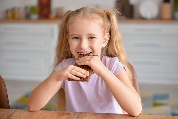 Милая маленькая девочка ест сладкий шоколад на кухне - Фото, изображение