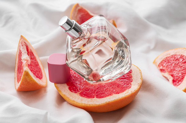 白い布の背景に香水とグレープフルーツのボトル、クローズアップ - 写真・画像
