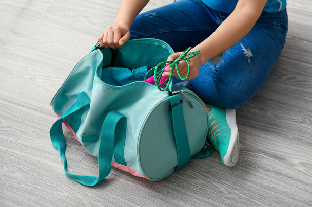 Woman in sport shoes preparing bag for training on light wooden floor - Photo, Image