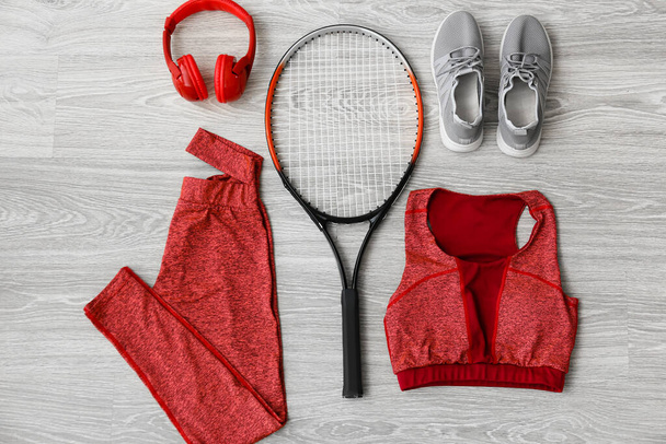 Sportbekleidung, Schuhe, Kopfhörer und Tennisschläger auf hellem Holzgrund - Foto, Bild