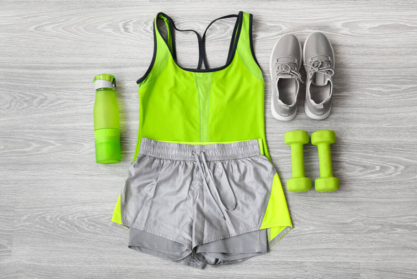 Vêtements de sport, chaussures, haltères et bouteille d'eau sur fond bois clair - Photo, image