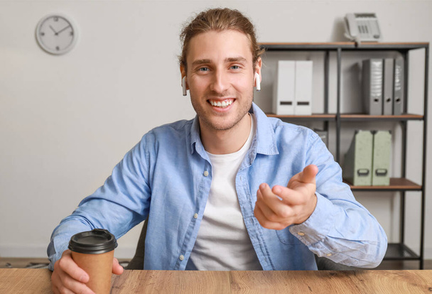 Handsome young man with cup of coffee video chatting in office - Photo, Image
