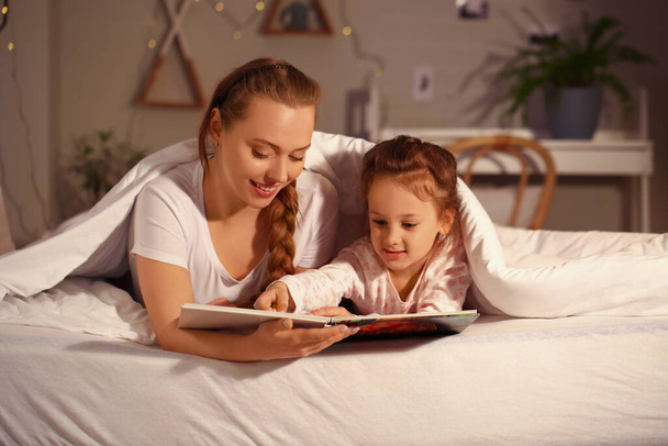 Klein meisje met haar moeder lezen bedtijd verhaal voor het slapen gaan - Foto, afbeelding