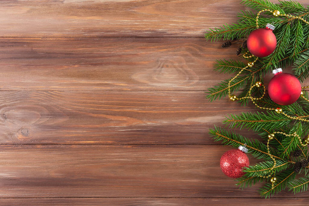 Tannenzweige mit roten Weihnachtskugeln und einem Kranz auf einem hölzernen Hintergrund. Weihnachten und Neujahr. Horizontale Ausrichtung, Kopierraum, Draufsicht. - Foto, Bild