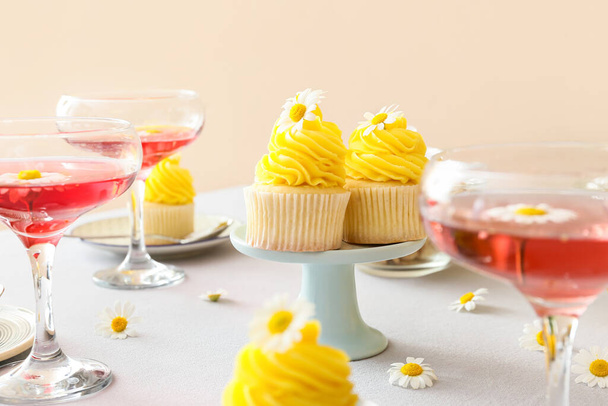 Tasty cupcakes, glasses of drink and chamomile flowers on table in room - Fotoğraf, Görsel