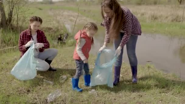 Mały dzieciak zbiera śmieci w zespole wolontariuszy, szczęśliwej rodzinie, sprząta ekologię ziemi ze śmieci, ekosystem, utrzymuje miejsca spoczynku w czystości, dziecko z matką sprząta - Materiał filmowy, wideo
