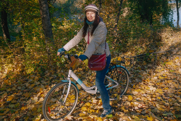 Beautiful young woman in a beret with long red hair is sitting on a bicycle in an autumn park. Around the fallen leave - Foto, imagen
