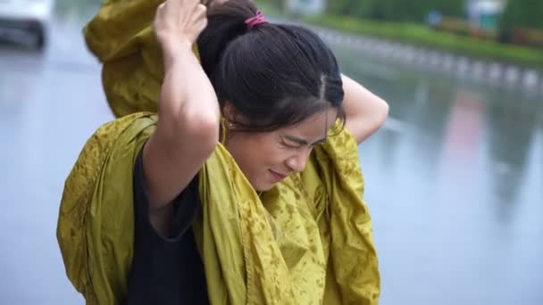 アジアの女の子は黄色のレインコートを急いでパーカーを着て、雨に雨が降り始め、雨季の気候は雨を注ぎ、仕事、ラッシュアワーの雨のために外出中に濡れると、雨の中で立ち往生 - 映像、動画