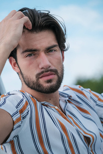 portrait of beautiful dark-haired italian model with light eyes and striped shirt with beard . High quality photo - Foto, Imagem